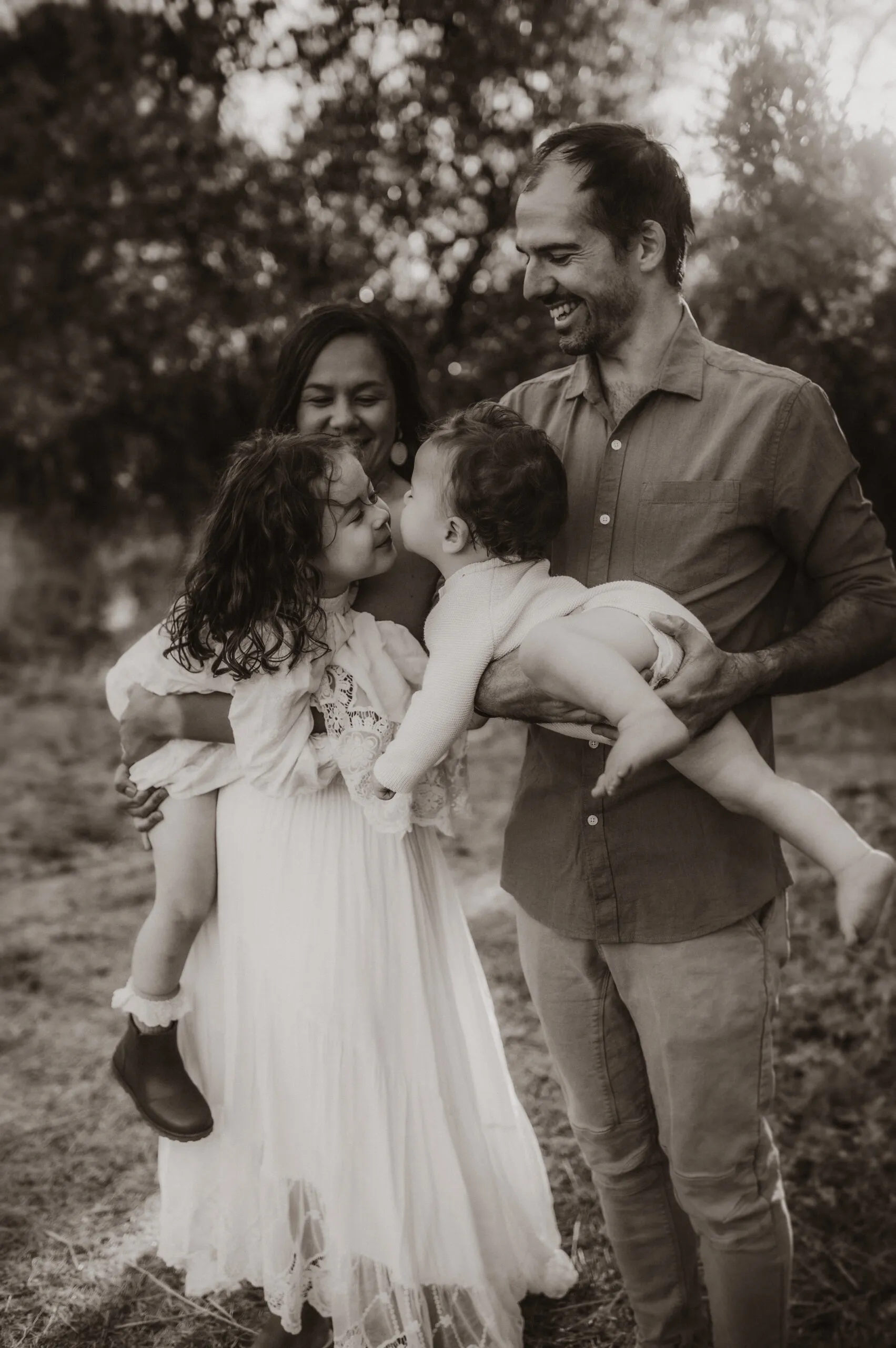 A smiling dad with two small children outdoors among soft golden trees