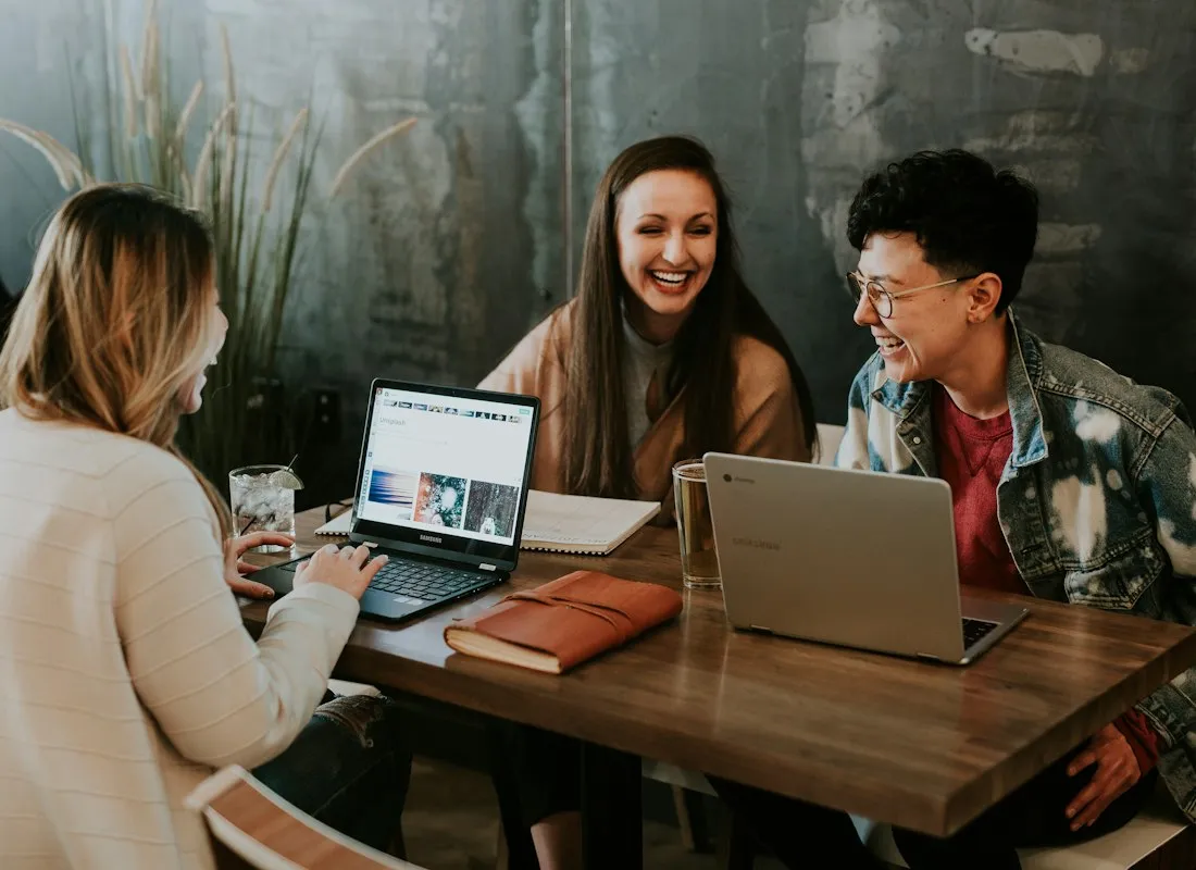 Three smiling people working on laptops around a table